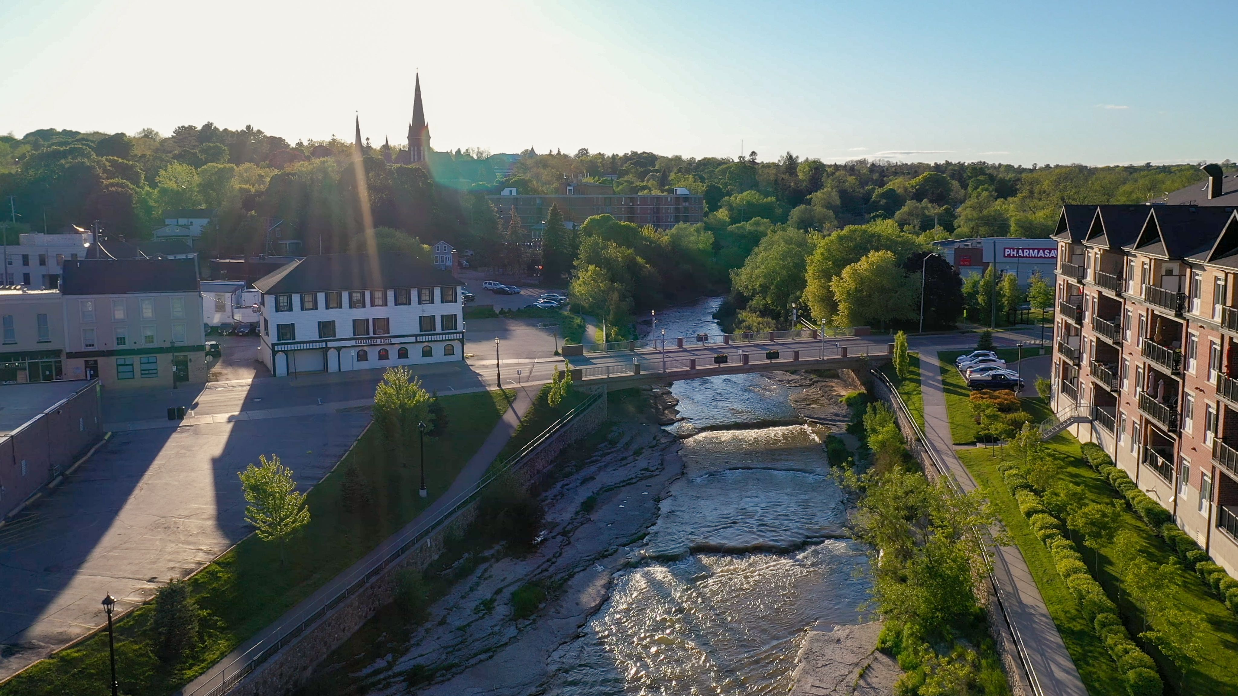The shining Ganaraska River flows through downtown Port hope, filled with aged green trees and historic brick buildings. The Ganaraska Hotel sits on the bank above the river.
